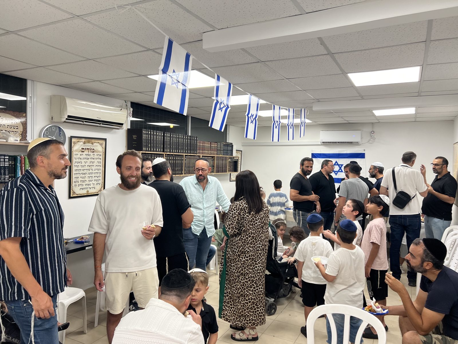 Vue large de la soirée d’accueil : drapeaux israéliens au plafond, adultes et enfants réunis