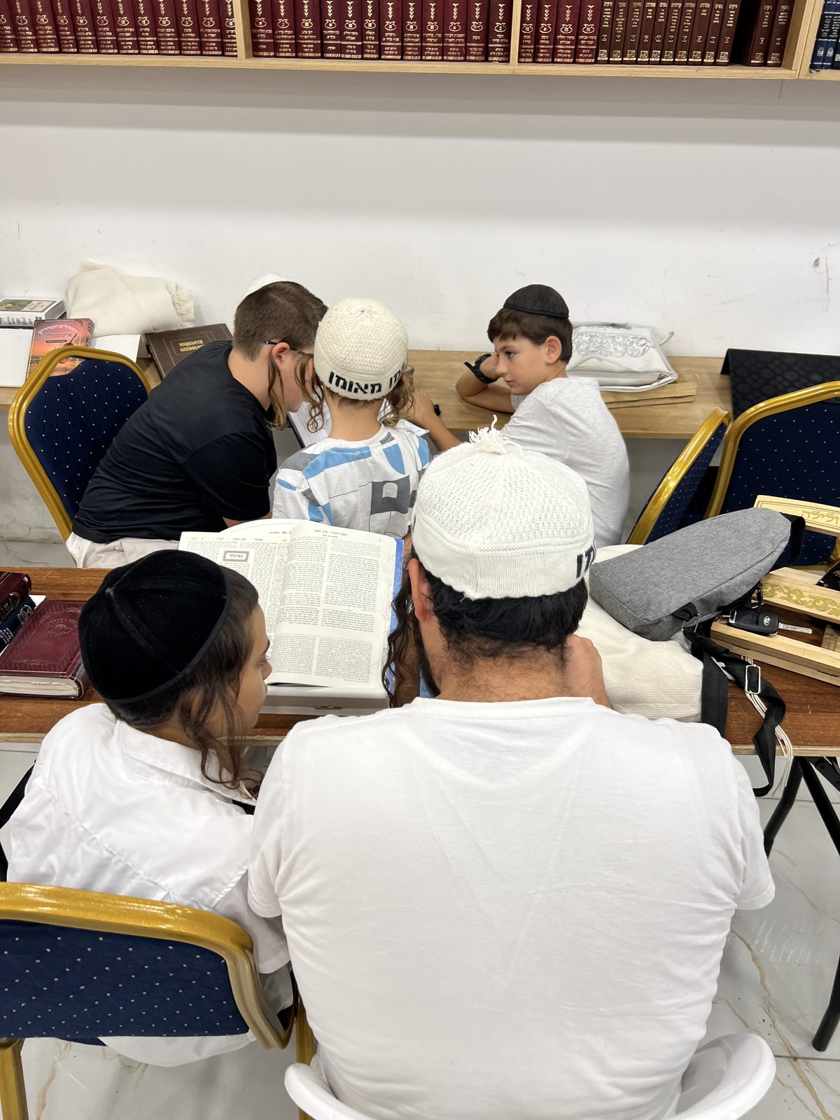 Enfants en kippa autour d’une guemara ouverte, étudiant avec leurs pères au beit midrash