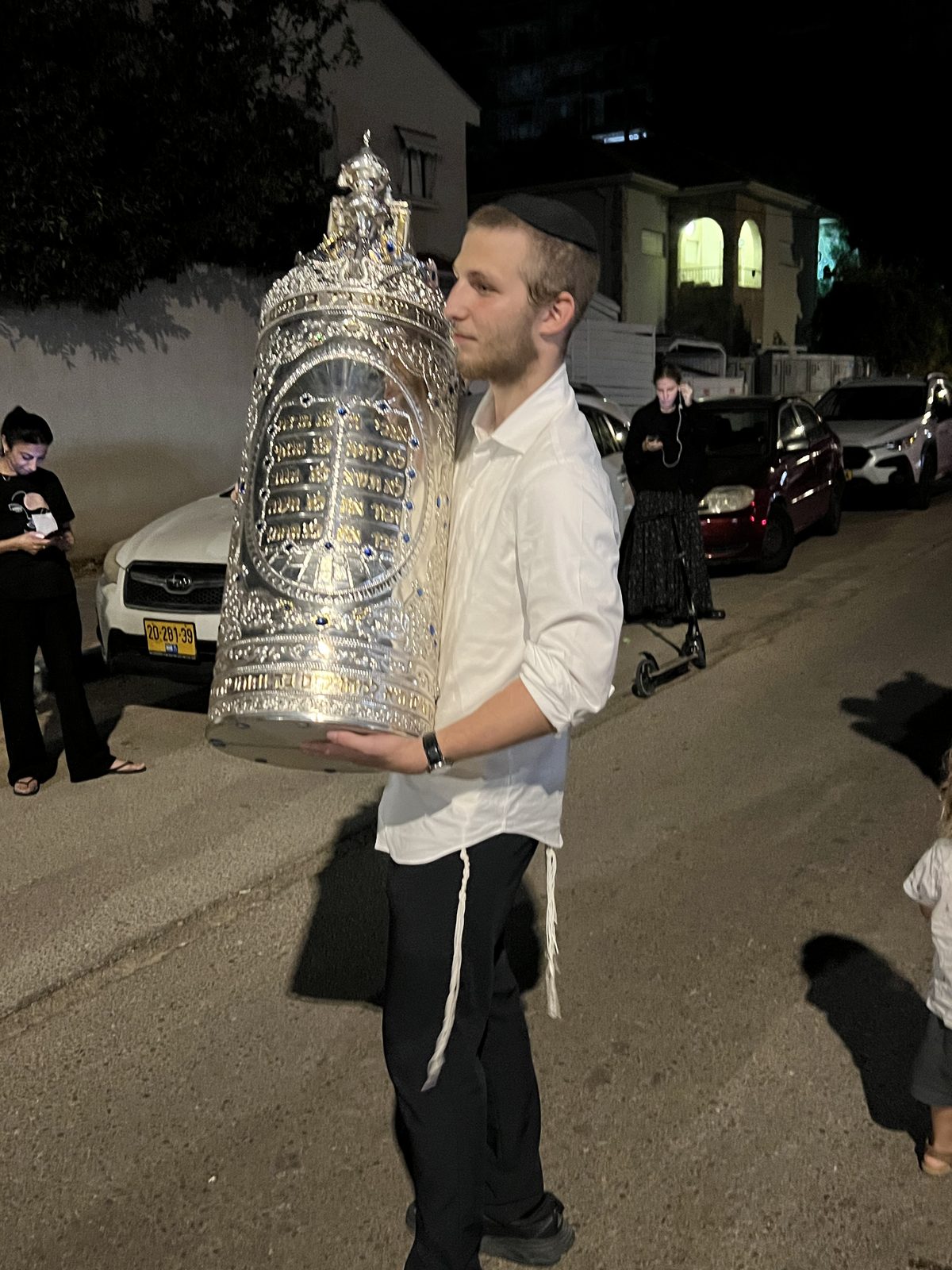 Jeune homme portant un sefer Torah à l’étui argenté dans la rue, de nuit