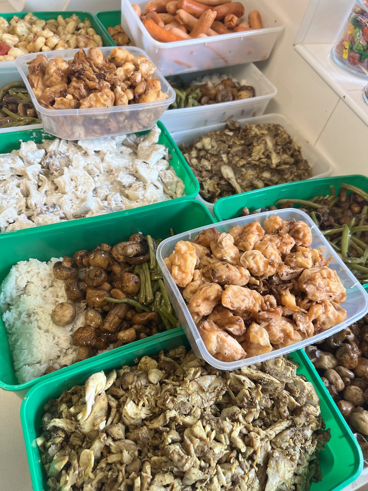 Barquettes de plats variés — riz, poulet en sauce, légumes — préparées en cuisine